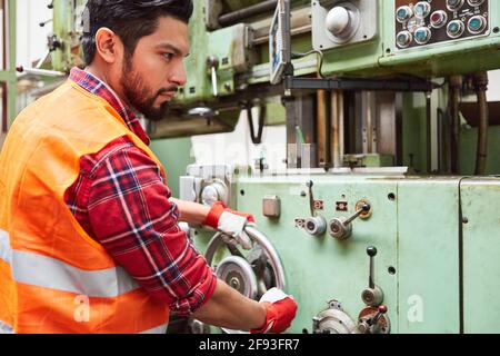 Worker in metal construction factory operates a drill press using a large wheel Stock Photo