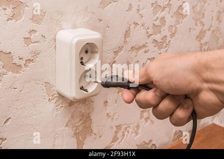 A man hand inserts or removes a plug from an outlet in a modern interior. Safe use of electrical appliances concept. Stock Photo