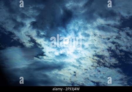 The full moon in the night sky hiding behind the clouds. Stock Photo