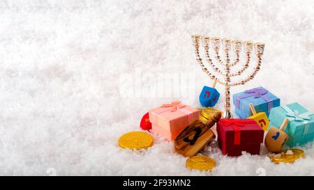 Jewish holiday and Hanukkah celebration with menorah, dreidel, gold coins or gelt and gifts on snow with copy space Stock Photo