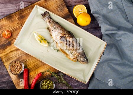 sea bass is served on a plate with lemon, against the background of a wooden table
