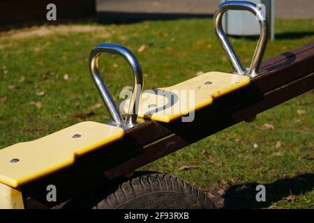 close up of a children's wooden seesaw with metal handles and yellow seats in a playground Stock Photo