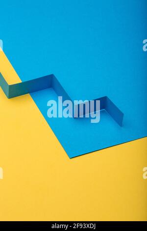 Abstract minimal paper background. Blue zig zag cut out paper stripe on blue and yellow paper background. Stock Photo