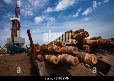 Oil deposit Zhaikmunai. Rig (derrick) left, and rusted drilling pipes right. Wide-angle view. Pipes caps in focus. Uralsk region, Kazakhstan. Stock Photo