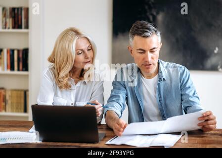 Brainstorm. Two successful and confident business partners in stylish clothes are sitting at the workplace, discussing, working on a new project, carefully reviewing and checking documents, use laptop Stock Photo