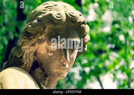 Weathered statue of an Angel with cracked dirty face at old cemetery - cross processed Stock Photo