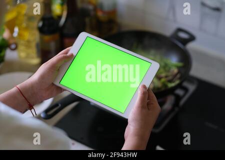 over shoulder view of woman holding green screen tablet when cooking in the kitchen Stock Photo