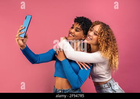 Stock photo of cheerful afro women posing while taking selfie in studio shot against pink background. Stock Photo
