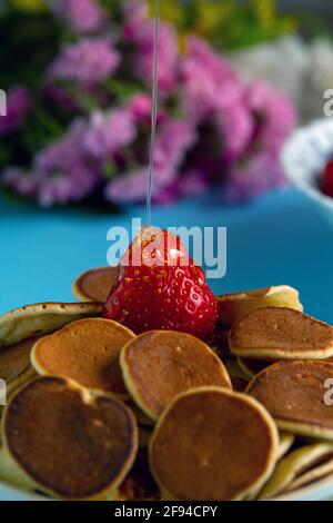 Strawberry lies in the midst of a mini pancakes, sprinkled with honey. Close-up. Selective focus. Stock Photo