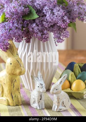 Bunch of lilac in a vase, wooden bunny family and colored eggs on an easter table. Vertical. Stock Photo