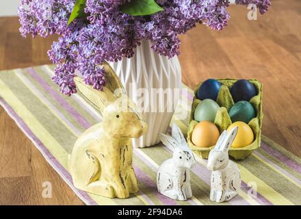 Bunch of lilac in a vase, wooden bunny family and colored eggs on an easter table. Vertical. Stock Photo