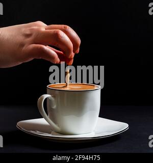 Woman's hand stirring a latte.This is a square-format photo taken on a black background under artificial light in a studio. Stock Photo