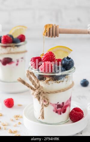 Yogurt with berries, cereals and honey in a glass on white background, vertical Stock Photo