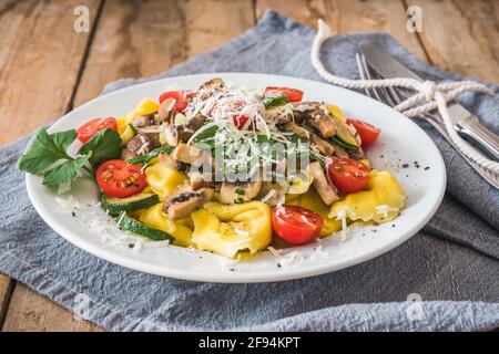 Italian cuisine: Tortellini with vegetarian mushroom cream sauce, zucchini,  fresh cherry tomatoes and parmesan cheese on a rustic wooden table Stock Photo