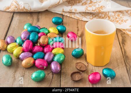 Cup of espresso and colorful wrapped easter chocolate eggs on a rustic wooden table Stock Photo