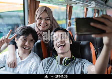 Three friends smile and pose in front of their cellphone camera while taking selfies Stock Photo