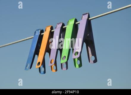 Low angle shot of multicolored cloth pins hanging on wire in outdoor with blue sky in background. Stock Photo