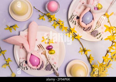 Easter table decorated with napkins and egg as an Easter bunny, egg candles and fresh forsythia branches, top view Stock Photo