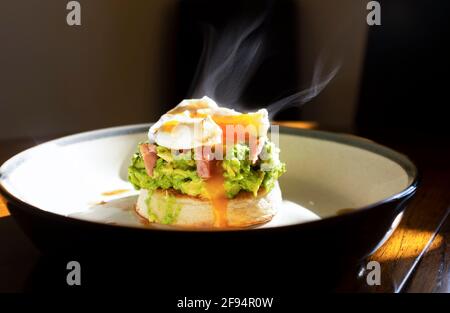 Crushed avocado and poached egg with ham pieces on a toasted crumpet for breakfast food UK Stock Photo