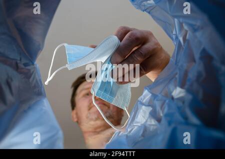 Defocus, blur, noise. Man throws medical mask into trash garbage can. Adult Man holding an unusable mask over a trash can indoors. Bottom view. Stock Photo