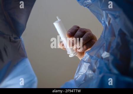 The hand throws the medical syringe into the trash. A man holds the unusable plastic syringe over an indoor trash can. Bottom view. Stock Photo