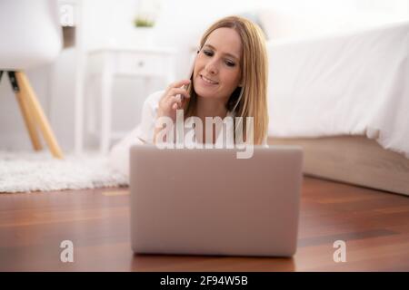 Beautiful woman lying on the floor with laptop talking on the phone Stock Photo