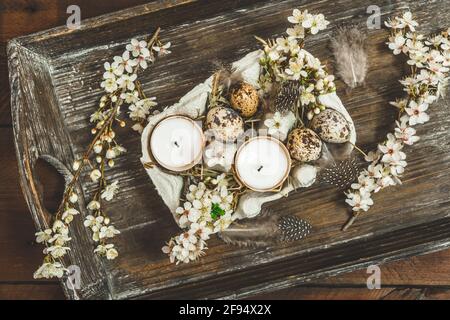 Candles in eggshells, quail eggs and white blossoming apple tree branches on a wooden tray as an Easter decoration, top view Stock Photo