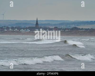 Storm-blown breakers rolling into Redcar Beach, seen from South Gare and with Coatham’s church and buildings, plus the Cleveland Hills as background. Stock Photo