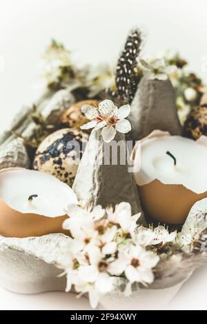 Candles in eggshells, quail eggs and white apple tree blossoms on a wooden tray as natural Easter decoration, vertical with white background Stock Photo