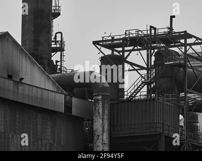A detail from the abandoned Redcar Steelworks complex, a flock of pigeons flying through a web of support structures and heavy pipe work. Stock Photo