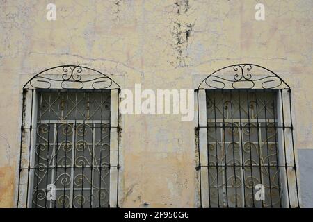 Colonial house facade with a faded Venetian stucco wall and stone trimmed windows with handcrafted iron grilles in Santiago de Querétaro, Mexico. Stock Photo