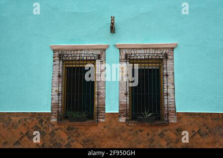 Colonial house facade with a Venetian stucco wall and stone trimmed windows with handcrafted iron grilles in Santiago de Querétaro, Mexico. Stock Photo