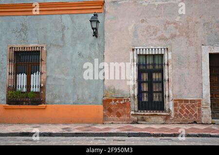 Colonial house facade with a Venetian stucco wall and stone trimmed windows with handcrafted iron grilles in Santiago de Querétaro, Mexico. Stock Photo