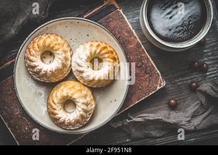 Three homemade mini bundt cakes on a plate, a cup of coffee and an old book on wooden background, top view Stock Photo