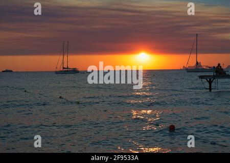 A beautiful sunset over the sea on the island of Formentera in Spain, with silhouettes of anchored sailboats and the sun on the horizon Stock Photo