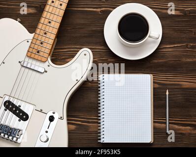 A cup of coffee, a guitar and a notebook on a dark wooden board. Stock Photo