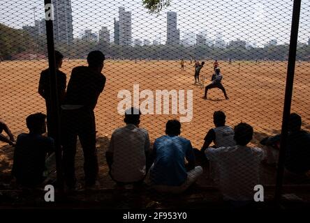 Silhouette of teenagers standing behind a fence watching a cricket match in Shivaji Park in Mumbai-Dadar,Maharashtra, India Stock Photo