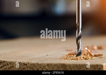 Drill bit makes hole in wood on a dark background. Stock Photo
