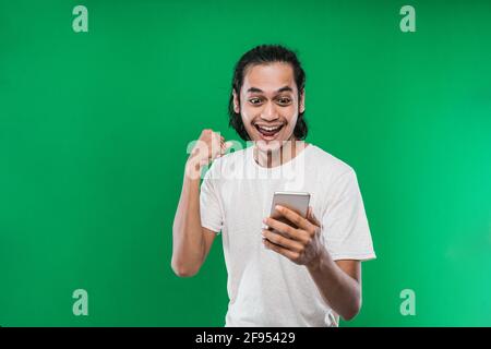 Asian man with long black hair holding and look handphone with happiness expression while raising one hand and making a fist Stock Photo