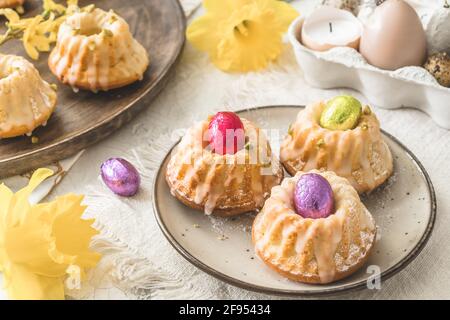 Homemade delicious mini lemon bundt cakes (muffins) and chocolate eggs on a easter table with fresh spring blossoms. Stock Photo