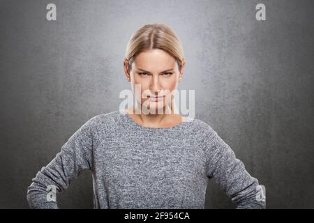Portrait of a very strict woman is looking at the camera. On a concrete gray background., Portrait of a very strict woman is looking at the camera. On