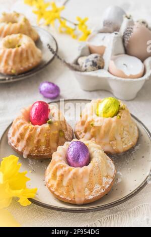 Homemade delicious mini lemon bundt cakes (muffins) and chocolate eggs on a easter table with fresh spring blossoms. Vertical. Stock Photo
