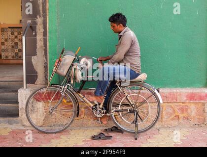 Knife grinder sitting on a bicycle sharpening a knife in Mumbai-Dadar, Maharashtra India,Asia. Stock Photo