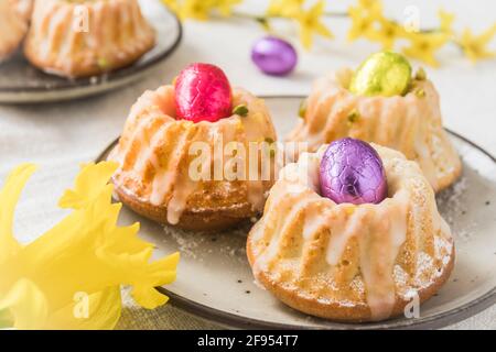 Homemade delicious mini lemon bundt cakes (muffins) with chocolate eggs on a table with spring blossoms. Stock Photo