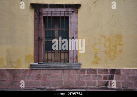 Colonial house facade with an faded ochre stucco wall and a stone trimmed window with handcrafted iron grilles in Santiago de Querétaro, Mexico. Stock Photo