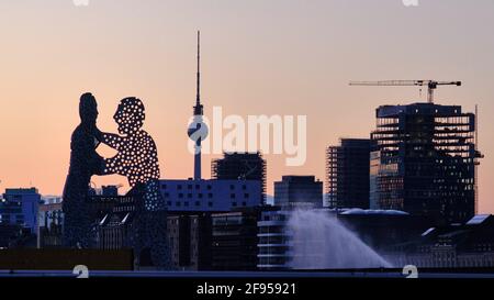 Berlin, Germany. 17th Mar, 2021. The sculpture 'Molecule Man' (l-r), the Berlin TV Tower and a new building form a panorama in the evening after sunset. The three-part monumental work stands in the Spree between Elsenbrücke and Oberbaumbrücke (rear), near the intersection of the three city districts of Kreuzberg, Treptow and Friedrichshain. Credit: Stefan Jaitner/dpa/Alamy Live News Stock Photo