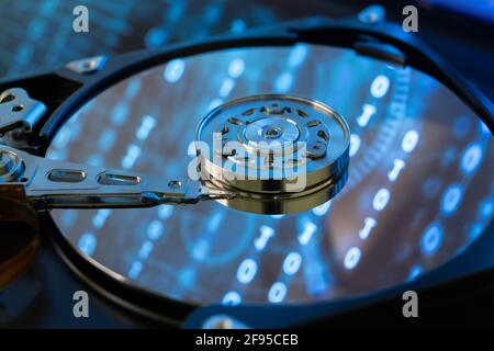 Inside of a hard disk HDD with binary code, zeros and ones, projected onto the surface. Bluish appearance. Stock Photo