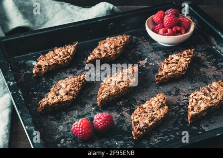 Homemade raspberry granola bars, decorated with raspberries, lying on a dark baking tray. Stock Photo