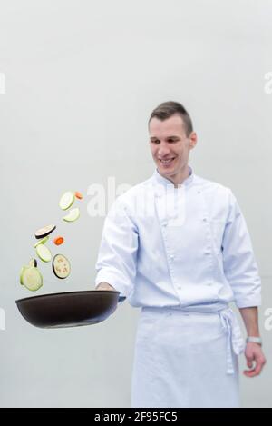 Happy young chef flipping vegetables in frying pan, healthy food concept Stock Photo