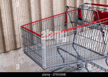 A silver and red metal shopping cart parked against a beige wall outside a supermarket in London, Ontario Canada on a gloomy and overcast day, winter. Stock Photo